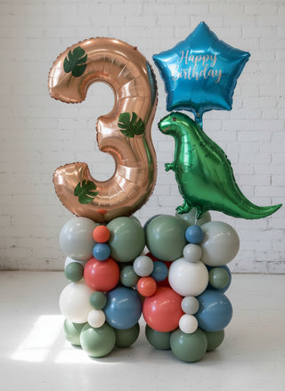 A balloon pedestal featuring a dinosaur shape with a 'Happy Birthday' balloon attached, surrounded by various colored balloons.