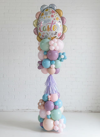 A decorative Easter-themed balloon tower with a variety of colorful balloons and Easter-themed foil decorations, standing upright on a floor.