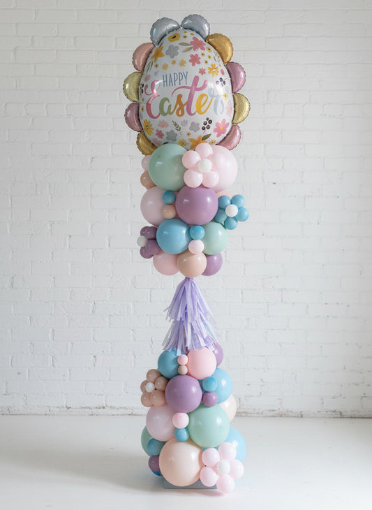 A decorative Easter-themed balloon tower with a variety of colorful balloons and Easter-themed foil decorations, standing upright on a floor.