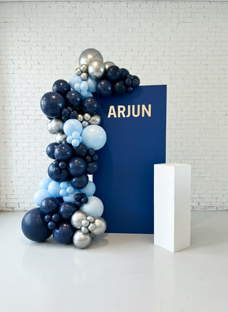 A custom event backdrop featuring the name ARJUN with blue, silver, and white balloons