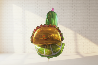 A set of three helium balloons arranged in the shape of a cactus, lime, and taco, with a pink flower on top, against a white paneled wall.