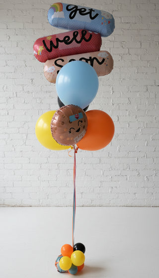 A get well soon helium bouquet with a variety of balloons in different colors and messages, approximately 5ft tall.