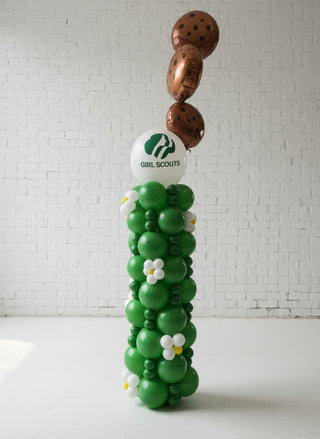 A balloon column decoration with a Girl Scout theme, featuring green and brown colors and a logo at the top.