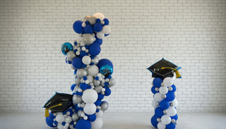 A freestanding garland and column balloon bundle decoration with a graduation theme, predominantly in shades of blue and white, with a graduation cap on top.