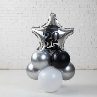 A tabletop graduation decoration featuring a silver balloon with the numbers 2025, surrounded by black and white balloons.