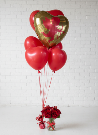 A helium balloon bouquet featuring a large gold heart-shaped balloon and smaller red heart-shaped balloons tied to a string, with a small red bow at the base.