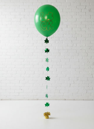 A large green balloon with a gold pattern resembling a leprechaun, attached to a string with smaller green shamrock decorations, displayed indoors.