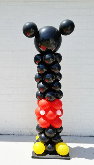 A balloon column decoration featuring the Mickey Mouse character design with black, red, and yellow balloons, standing upright against a wall.