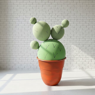 A hand-designed artificial cactus in a orange pot, with a green body and a whimsical shape, placed indoors.