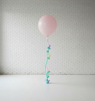 A pink balloon with a decorative ribbon and handmade flowers attached, against a neutral background.