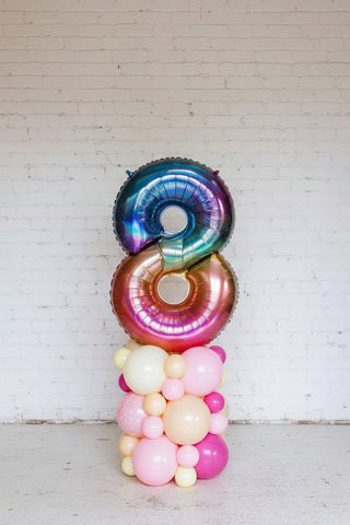 A multicolored balloon column featuring a spiral design with a mix of large and small balloons, including metallic and plain styles, set against a white background.