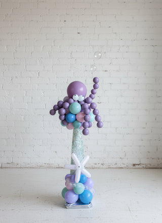 A centerpiece featuring a deep sea octopus with purple and blue balloons, placed against a light-colored wall.