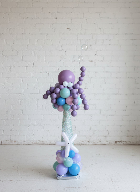 A centerpiece featuring a deep sea octopus with purple and blue balloons, placed against a light-colored wall.