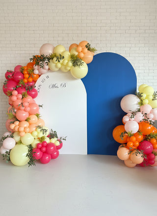 An engagement party backdrop with pink, organge, and yellow ballons and greenery
