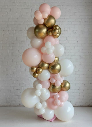 A free standing garland featuring a variety of balloons in pink, gold, and white colors, arranged in a spiral pattern.