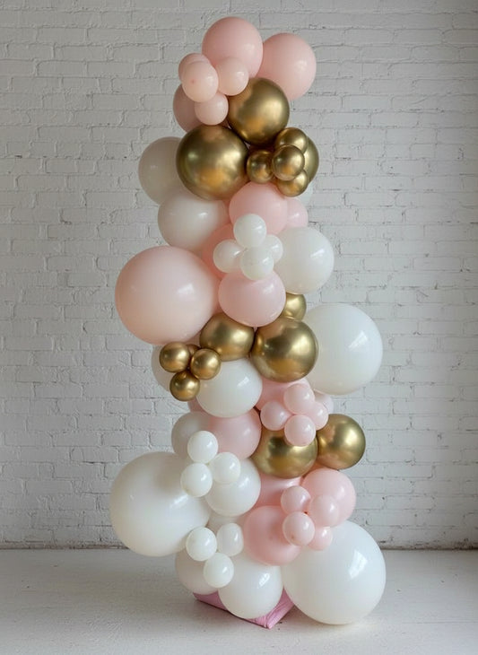A free standing garland featuring a variety of balloons in pink, gold, and white colors, arranged in a spiral pattern.