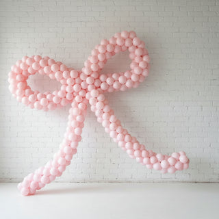 Large pink balloon bow against a white brick wall