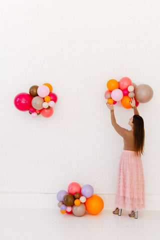 Woman arranging colorful balloons against a white wall