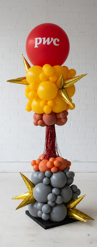 A colorful balloon tower with a variety of balloons in different shapes and colors, including a large red balloon at the top, standing upright on a flat surface.
