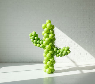 A life-sized balloon cactus decoration with green bodies and two artificial flowers in pink and orange colors.