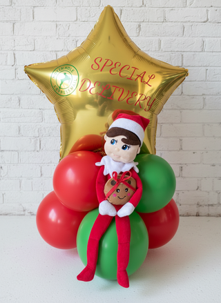 A figurine of an elf sitting on a balloon bouquet with a 'Special Delivery' balloon in the background.