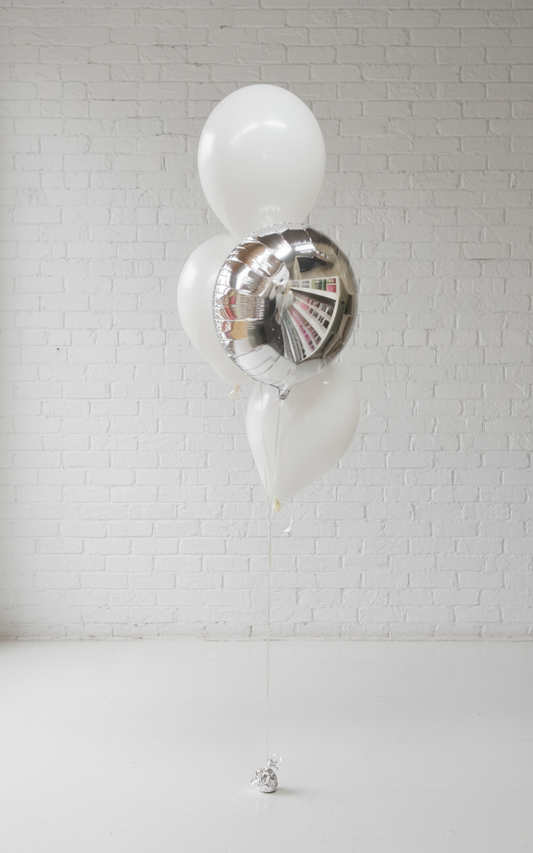 A helium balloon bouquet featuring a large silver foil balloon, with three white latex balloons, arranged to stand upright against a plain background.