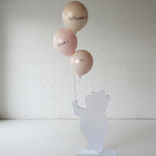 A customizable foam cutout welcome sign with a silhouette of a bear, accompanied by two helium balloons placed against a wall.