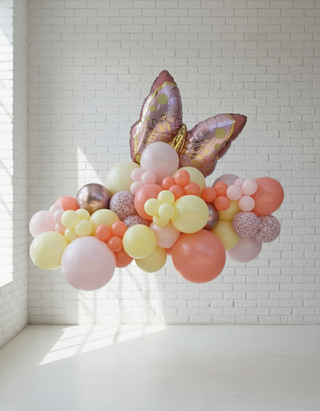 A colorful balloon garland featuring a variety of colors including pink, gold, and yellow, shaped into a semi-circular form with an Easter egg and butterfly design, displayed against a white wall.