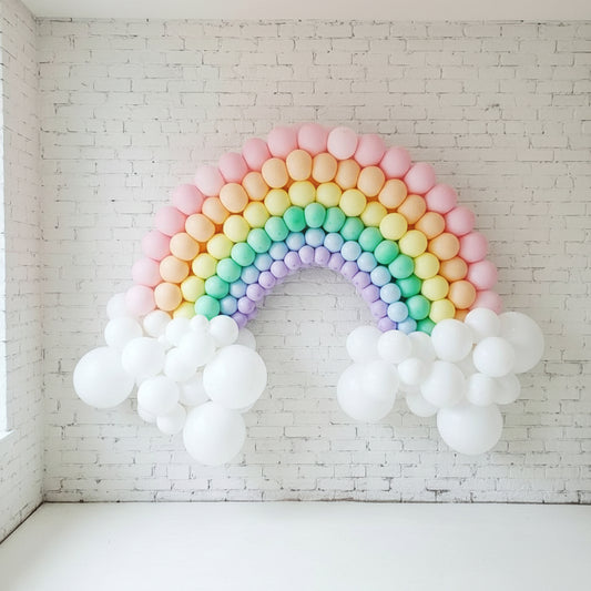A balloon sculpture designed in the shape of a rainbow with multicolored balloons and white clouds, attached to a wall as a backdrop.